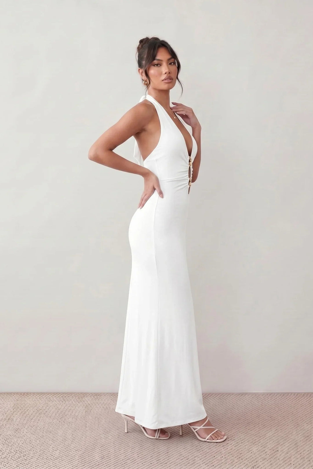 Woman wearing the Ariadna Mermaid Halter Maxi Dress featuring a deep plunge halter neckline, open back with adjustable tie fastening, gold-tone hardware at the ruched waist, subtle waist cut-out and a floor-length mermaid silhouette, ideal for weddings, black-tie events and formal evening occasions.