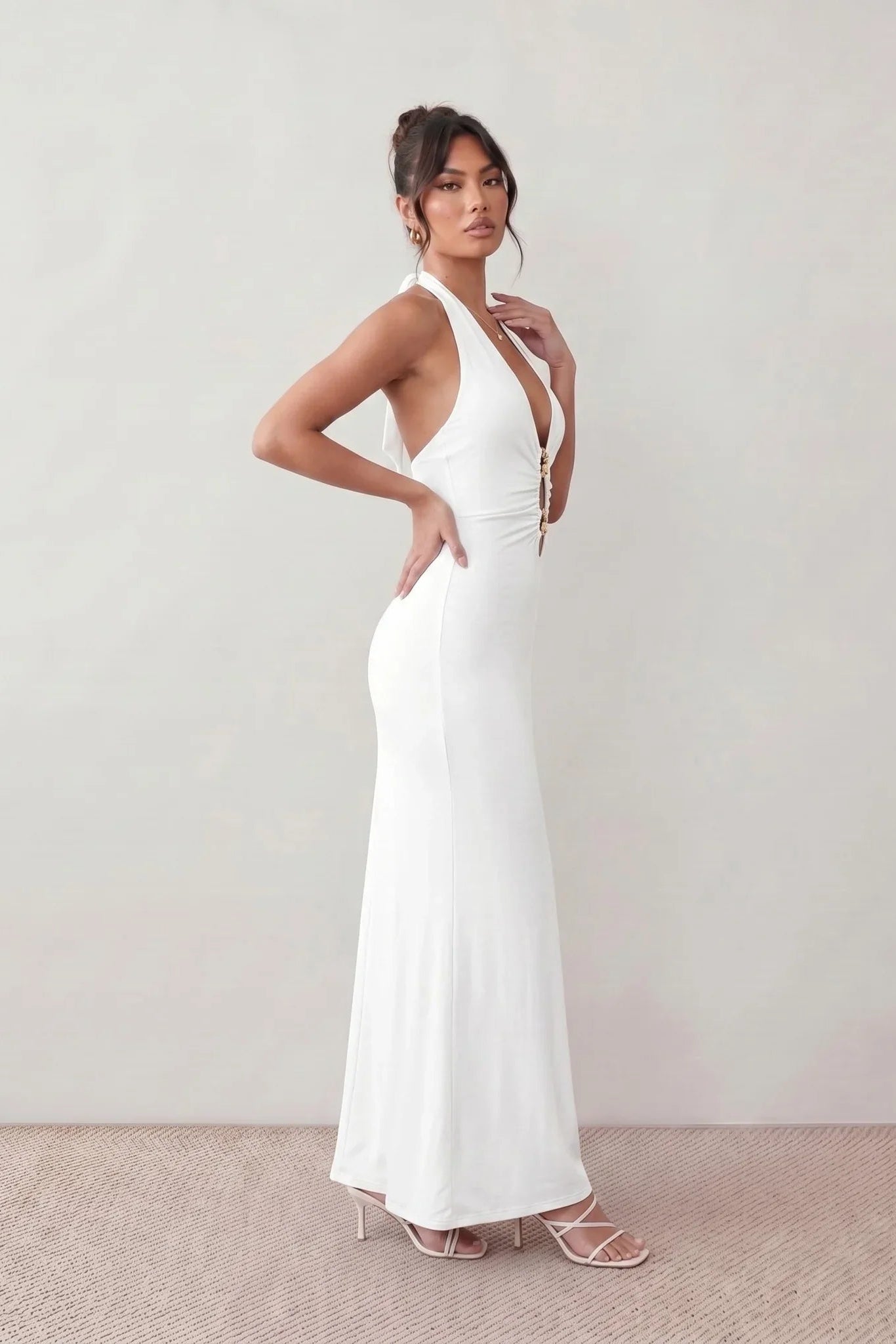 Woman wearing the Ariadna Mermaid Halter Maxi Dress featuring a deep plunge halter neckline, open back with adjustable tie fastening, gold-tone hardware at the ruched waist, subtle waist cut-out and a floor-length mermaid silhouette, ideal for weddings, black-tie events and formal evening occasions.