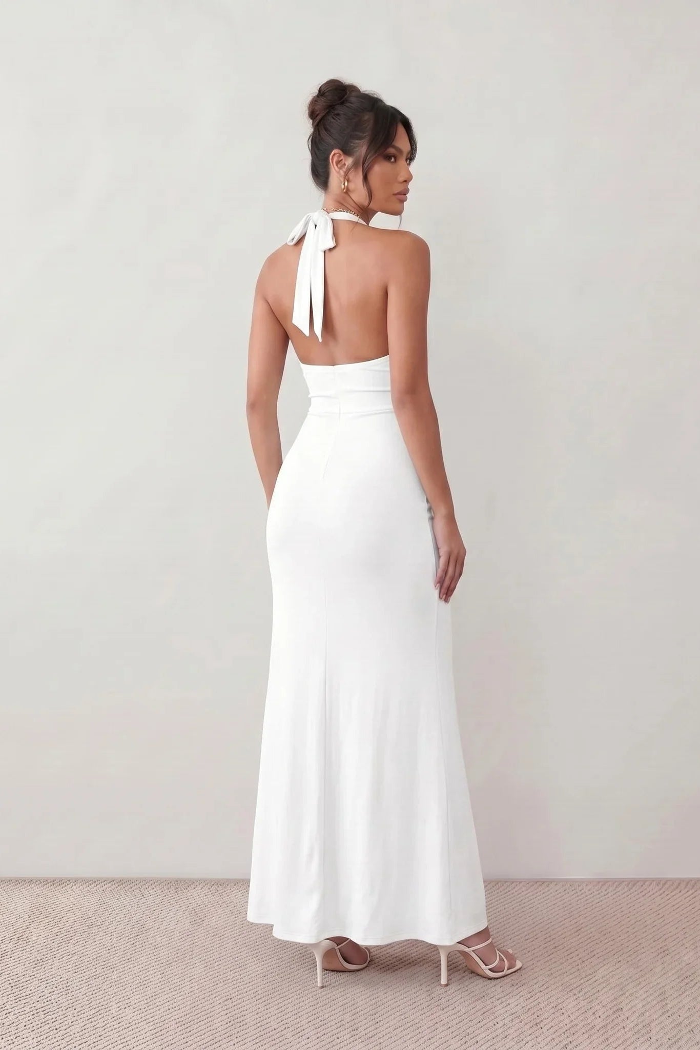 Woman wearing the Ariadna Mermaid Halter Maxi Dress featuring a deep plunge halter neckline, open back with adjustable tie fastening, gold-tone hardware at the ruched waist, subtle waist cut-out and a floor-length mermaid silhouette, ideal for weddings, black-tie events and formal evening occasions.