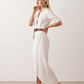 Woman wearing the Julieta Button Front Maxi Dress with a deep V-neck, shirt collar, button-front bodice, long sleeves, belted waist with a square-buckle belt, asymmetric pleated hip drape, and flowing maxi-length skirt.