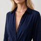 Woman wearing the Julieta Button Front Maxi Dress with a deep V-neck, shirt collar, button-front bodice, long sleeves, belted waist with a square-buckle belt, asymmetric pleated hip drape, and flowing maxi-length skirt.