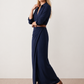 Woman wearing the Julieta Button Front Maxi Dress with a deep V-neck, shirt collar, button-front bodice, long sleeves, belted waist with a square-buckle belt, asymmetric pleated hip drape, and flowing maxi-length skirt.