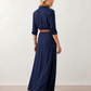 Woman wearing the Julieta Button Front Maxi Dress with a deep V-neck, shirt collar, button-front bodice, long sleeves, belted waist with a square-buckle belt, asymmetric pleated hip drape, and flowing maxi-length skirt.