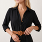 Woman wearing the Julieta Button Front Maxi Dress with a deep V-neck, shirt collar, button-front bodice, long sleeves, belted waist with a square-buckle belt, asymmetric pleated hip drape, and flowing maxi-length skirt.