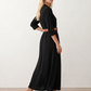 Woman wearing the Julieta Button Front Maxi Dress with a deep V-neck, shirt collar, button-front bodice, long sleeves, belted waist with a square-buckle belt, asymmetric pleated hip drape, and flowing maxi-length skirt.