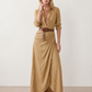 Woman wearing the Julieta Button Front Maxi Dress with a deep V-neck, shirt collar, button-front bodice, long sleeves, belted waist with a square-buckle belt, asymmetric pleated hip drape, and flowing maxi-length skirt.