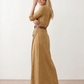 Woman wearing the Julieta Button Front Maxi Dress with a deep V-neck, shirt collar, button-front bodice, long sleeves, belted waist with a square-buckle belt, asymmetric pleated hip drape, and flowing maxi-length skirt.