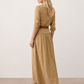 Woman wearing the Julieta Button Front Maxi Dress with a deep V-neck, shirt collar, button-front bodice, long sleeves, belted waist with a square-buckle belt, asymmetric pleated hip drape, and flowing maxi-length skirt.