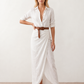 Woman wearing the Julieta Button Front Maxi Dress with a deep V-neck, shirt collar, button-front bodice, long sleeves, belted waist with a square-buckle belt, asymmetric pleated hip drape, and flowing maxi-length skirt.