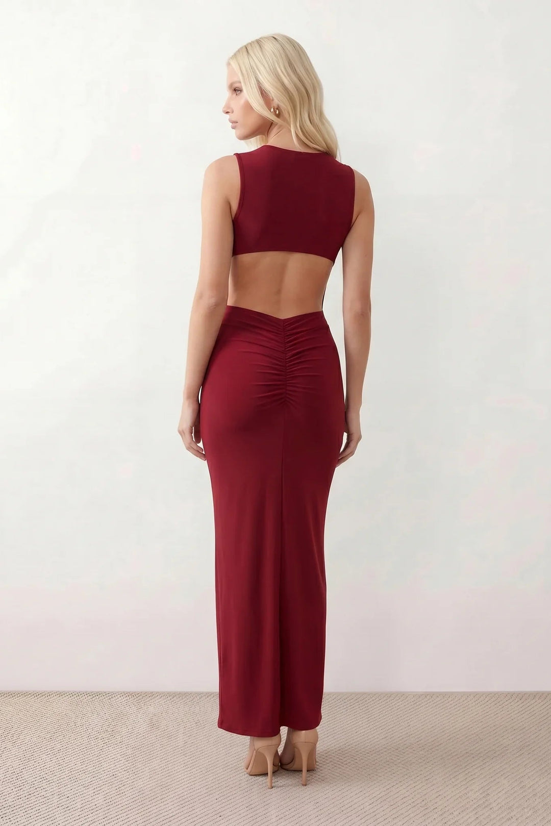 Woman wearing the Calista Open Back Fitted Maxi Dress in a fitted floor-length silhouette featuring a round neckline, sleeveless design, dramatic open back, ruched waist, gold-tone buckle detail at the hip, and a subtle mermaid hem, perfect for weddings, black-tie events and formal occasions.