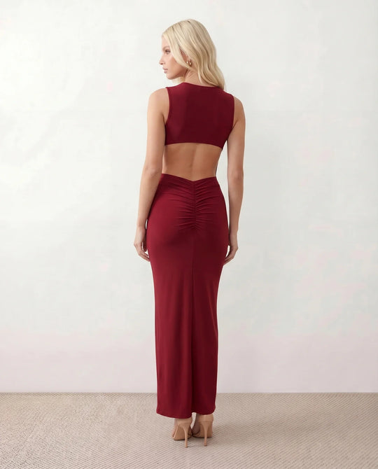 Woman wearing the Calista Open Back Fitted Maxi Dress in a fitted floor-length silhouette featuring a round neckline, sleeveless design, dramatic open back, ruched waist, gold-tone buckle detail at the hip, and a subtle mermaid hem, perfect for weddings, black-tie events and formal occasions.