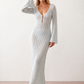 Woman wearing the Calixta Crochet Plunge Neck Maxi Dress in an elegant open-knit crochet design with a deep plunge V-neck, keyhole detail, long flared sleeves, low open back and fitted floor-length silhouette, ideal for beach holidays, festivals and summer occasion wear.