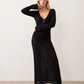 Woman wearing the Calixta Crochet Plunge Neck Maxi Dress in an elegant open-knit crochet design with a deep plunge V-neck, keyhole detail, long flared sleeves, low open back and fitted floor-length silhouette, ideal for beach holidays, festivals and summer occasion wear.
