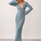 Woman wearing the Calixta Crochet Plunge Neck Maxi Dress in an elegant open-knit crochet design with a deep plunge V-neck, keyhole detail, long flared sleeves, low open back and fitted floor-length silhouette, ideal for beach holidays, festivals and summer occasion wear.
