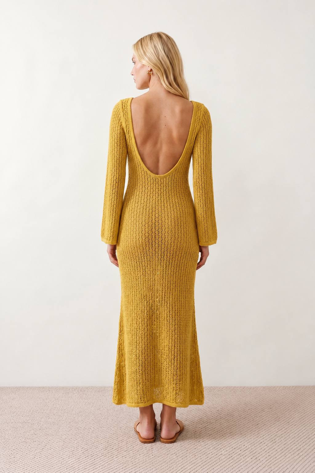 Woman wearing the Calixta Crochet Plunge Neck Maxi Dress in an elegant open-knit crochet design with a deep plunge V-neck, keyhole detail, long flared sleeves, low open back and fitted floor-length silhouette, ideal for beach holidays, festivals and summer occasion wear.