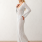 Woman wearing the Calixta Crochet Plunge Neck Maxi Dress in an elegant open-knit crochet design with a deep plunge V-neck, keyhole detail, long flared sleeves, low open back and fitted floor-length silhouette, ideal for beach holidays, festivals and summer occasion wear.