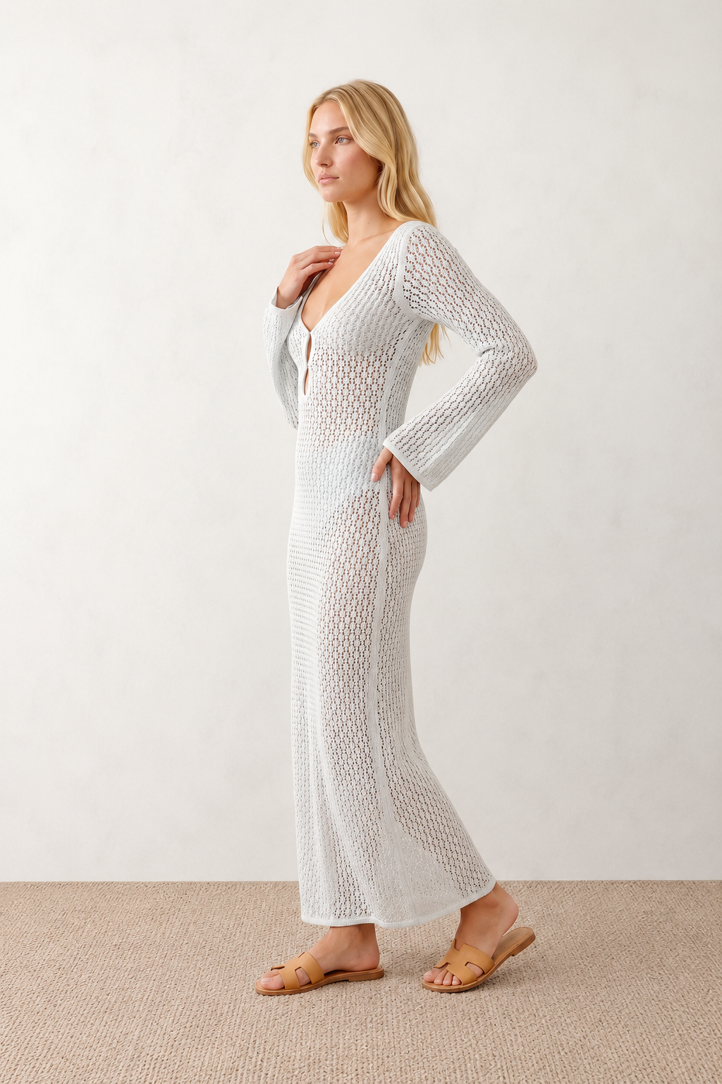 Woman wearing the Calixta Crochet Plunge Neck Maxi Dress in an elegant open-knit crochet design with a deep plunge V-neck, keyhole detail, long flared sleeves, low open back and fitted floor-length silhouette, ideal for beach holidays, festivals and summer occasion wear.