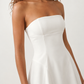 Woman wearing the Camilla Strapless Pleated Mini Dress featuring a structured strapless square neckline, fitted bodice, softly pleated A-line mini skirt, natural waist, and concealed back zip, styled for weddings, cocktail parties, race days, and special occasions.