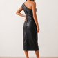 Woman wearing the Celia Faux Leather Glossy Midi Dress in high-shine faux leather, featuring an asymmetric off-the-shoulder draped neckline, fitted pencil silhouette, ruched waist, low-back design with concealed zip fastening, back slit, and elegant midi length, styled for cocktail parties and evening occasions.
