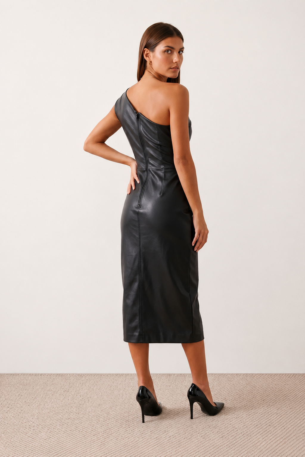 Woman wearing the Celia Faux Leather Glossy Midi Dress in high-shine faux leather, featuring an asymmetric off-the-shoulder draped neckline, fitted pencil silhouette, ruched waist, low-back design with concealed zip fastening, back slit, and elegant midi length, styled for cocktail parties and evening occasions.