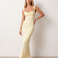 Woman wearing the Aline Cowl Neck Backless Maxi Dress in a floor-length fitted silhouette with a draped cowl neckline, elegant open back, oversized satin bow tie detail, sleeveless design, and smooth woven fabric, ideal for weddings, black-tie events, galas, and evening occasions.