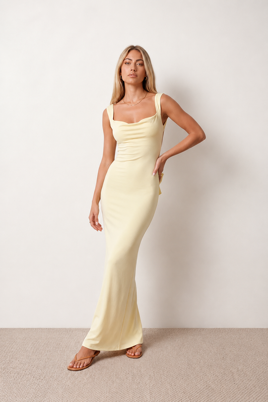 Woman wearing the Aline Cowl Neck Backless Maxi Dress in a floor-length fitted silhouette with a draped cowl neckline, elegant open back, oversized satin bow tie detail, sleeveless design, and smooth woven fabric, ideal for weddings, black-tie events, galas, and evening occasions.