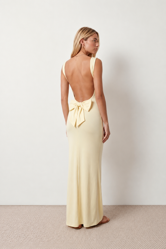 Woman wearing the Aline Cowl Neck Backless Maxi Dress in a floor-length fitted silhouette with a draped cowl neckline, elegant open back, oversized satin bow tie detail, sleeveless design, and smooth woven fabric, ideal for weddings, black-tie events, galas, and evening occasions.