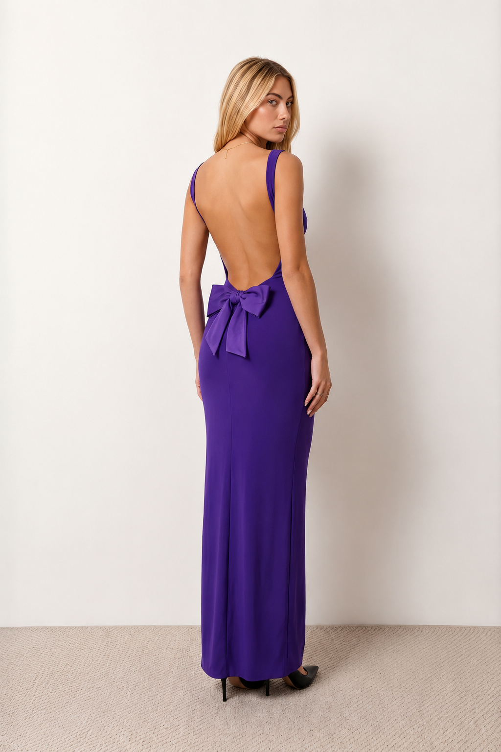 Woman wearing the Aline Cowl Neck Backless Maxi Dress in a floor-length fitted silhouette with a draped cowl neckline, elegant open back, oversized satin bow tie detail, sleeveless design, and smooth woven fabric, ideal for weddings, black-tie events, galas, and evening occasions.