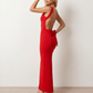 Woman wearing the Aline Cowl Neck Backless Maxi Dress in a floor-length fitted silhouette with a draped cowl neckline, elegant open back, oversized satin bow tie detail, sleeveless design, and smooth woven fabric, ideal for weddings, black-tie events, galas, and evening occasions.