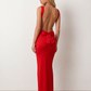 Woman wearing the Aline Cowl Neck Backless Maxi Dress in a floor-length fitted silhouette with a draped cowl neckline, elegant open back, oversized satin bow tie detail, sleeveless design, and smooth woven fabric, ideal for weddings, black-tie events, galas, and evening occasions.