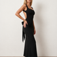 Woman wearing the Aline Cowl Neck Backless Maxi Dress in a floor-length fitted silhouette with a draped cowl neckline, elegant open back, oversized satin bow tie detail, sleeveless design, and smooth woven fabric, ideal for weddings, black-tie events, galas, and evening occasions.