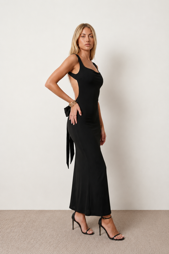 Woman wearing the Aline Cowl Neck Backless Maxi Dress in a floor-length fitted silhouette with a draped cowl neckline, elegant open back, oversized satin bow tie detail, sleeveless design, and smooth woven fabric, ideal for weddings, black-tie events, galas, and evening occasions.