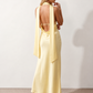 Aleena cowl neck halter maxi dress with a deep draped neckline, fitted halter strap, open back with tie-neck closure, sleeveless column silhouette, and floor-length straight hem in a smooth, elegant finish.