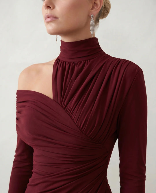 Woman wearing the Felisa Asymmetric Neck Open Back Midi Dress featuring an asymmetric mock-neck halter, off-shoulder ruched detailing, long fitted sleeves, an elegant open back, fitted midi silhouette and front slit, styled for weddings, cocktail parties and formal occasions.