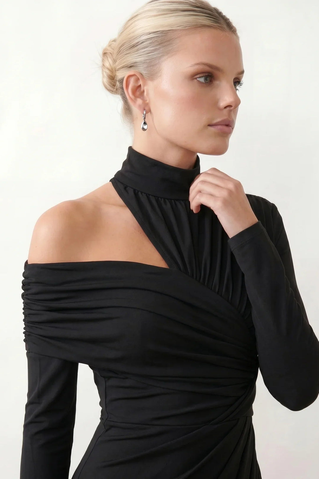 Woman wearing the Felisa Asymmetric Neck Open Back Midi Dress featuring an asymmetric mock-neck halter, off-shoulder ruched detailing, long fitted sleeves, an elegant open back, fitted midi silhouette and front slit, styled for weddings, cocktail parties and formal occasions.