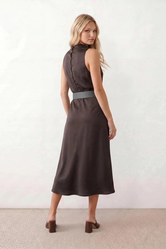 Woman wearing the  glossy cowl neck belted midi dress featuring a draped neckline, sleeveless sheath silhouette, removable wide buckle belt, and elegant midi-length hem in a lustrous finish.