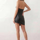 Woman wearing a glossy faux leather halter mini dress with a draped cowl neckline, fully backless design, ruched waist and hips, bodycon fit, and an asymmetric mini hem, styled for parties, cocktail events, and evening occasions.