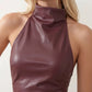 Woman wearing a glossy faux leather halter mini dress with a draped cowl neckline, fully backless design, ruched waist and hips, bodycon fit, and an asymmetric mini hem, styled for parties, cocktail events, and evening occasions.