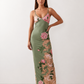 Woman wearing the Milota glossy floral slip maxi dress featuring a baroque-inspired floral print, deep V-neckline, adjustable spaghetti straps, low draped back, satin-look finish, and body-skimming floor-length silhouette, ideal for wedding guests and formal occasions.