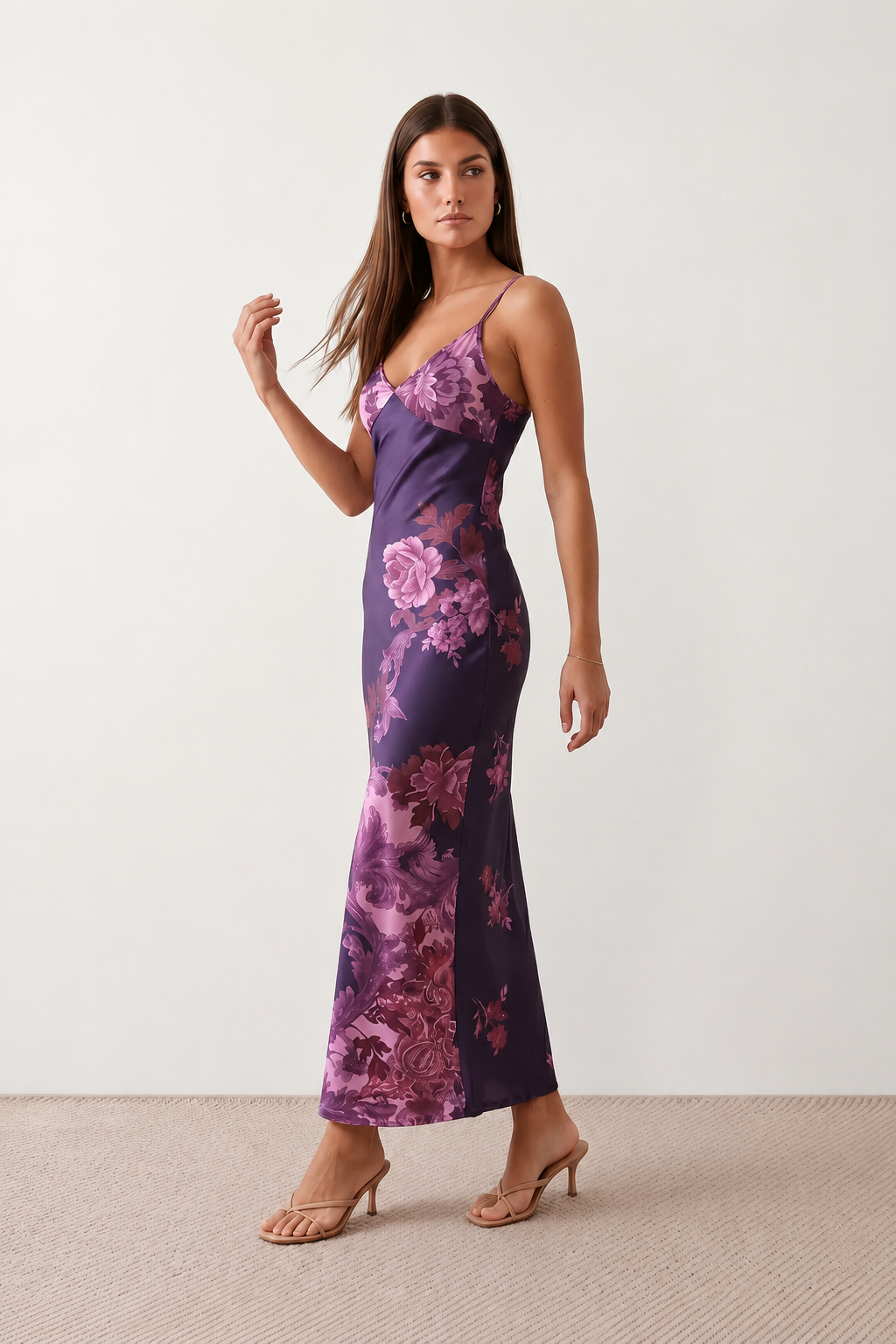 Woman wearing the Milota glossy floral slip maxi dress featuring a baroque-inspired floral print, deep V-neckline, adjustable spaghetti straps, low draped back, satin-look finish, and body-skimming floor-length silhouette, ideal for wedding guests and formal occasions.