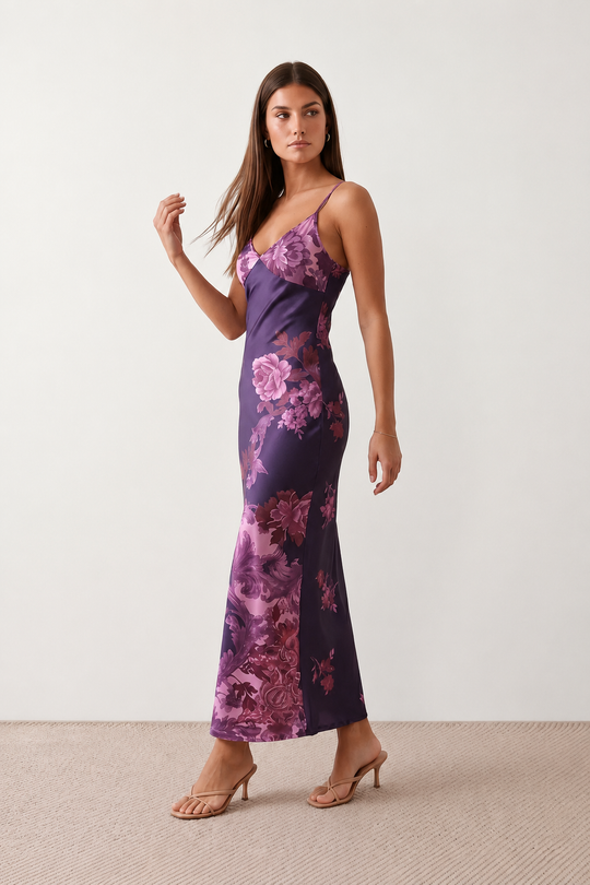 Woman wearing the Milota glossy floral slip maxi dress featuring a baroque-inspired floral print, deep V-neckline, adjustable spaghetti straps, low draped back, satin-look finish, and body-skimming floor-length silhouette, ideal for wedding guests and formal occasions.