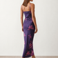 Woman wearing the Milota glossy floral slip maxi dress featuring a baroque-inspired floral print, deep V-neckline, adjustable spaghetti straps, low draped back, satin-look finish, and body-skimming floor-length silhouette, ideal for wedding guests and formal occasions.