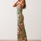 Woman wearing the Milota glossy floral slip maxi dress featuring a baroque-inspired floral print, deep V-neckline, adjustable spaghetti straps, low draped back, satin-look finish, and body-skimming floor-length silhouette, ideal for wedding guests and formal occasions.