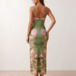 Woman wearing the Milota glossy floral slip maxi dress featuring a baroque-inspired floral print, deep V-neckline, adjustable spaghetti straps, low draped back, satin-look finish, and body-skimming floor-length silhouette, ideal for wedding guests and formal occasions.