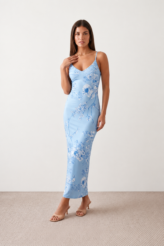 Woman wearing the Milota glossy floral slip maxi dress featuring a baroque-inspired floral print, deep V-neckline, adjustable spaghetti straps, low draped back, satin-look finish, and body-skimming floor-length silhouette, ideal for wedding guests and formal occasions.