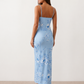 Woman wearing the Milota glossy floral slip maxi dress featuring a baroque-inspired floral print, deep V-neckline, adjustable spaghetti straps, low draped back, satin-look finish, and body-skimming floor-length silhouette, ideal for wedding guests and formal occasions.