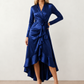 Woman wearing the Cordula Glossy Ruffle Detail Maxi Dress in a satin-look finish featuring a wrap V-neckline, long sleeves, self-tie waist sash and cascading asymmetric ruffle high-low hem, styled as an elegant wedding guest and occasion dress.