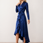 Woman wearing the Cordula Glossy Ruffle Detail Maxi Dress in a satin-look finish featuring a wrap V-neckline, long sleeves, self-tie waist sash and cascading asymmetric ruffle high-low hem, styled as an elegant wedding guest and occasion dress.