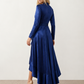 Woman wearing the Cordula Glossy Ruffle Detail Maxi Dress in a satin-look finish featuring a wrap V-neckline, long sleeves, self-tie waist sash and cascading asymmetric ruffle high-low hem, styled as an elegant wedding guest and occasion dress.