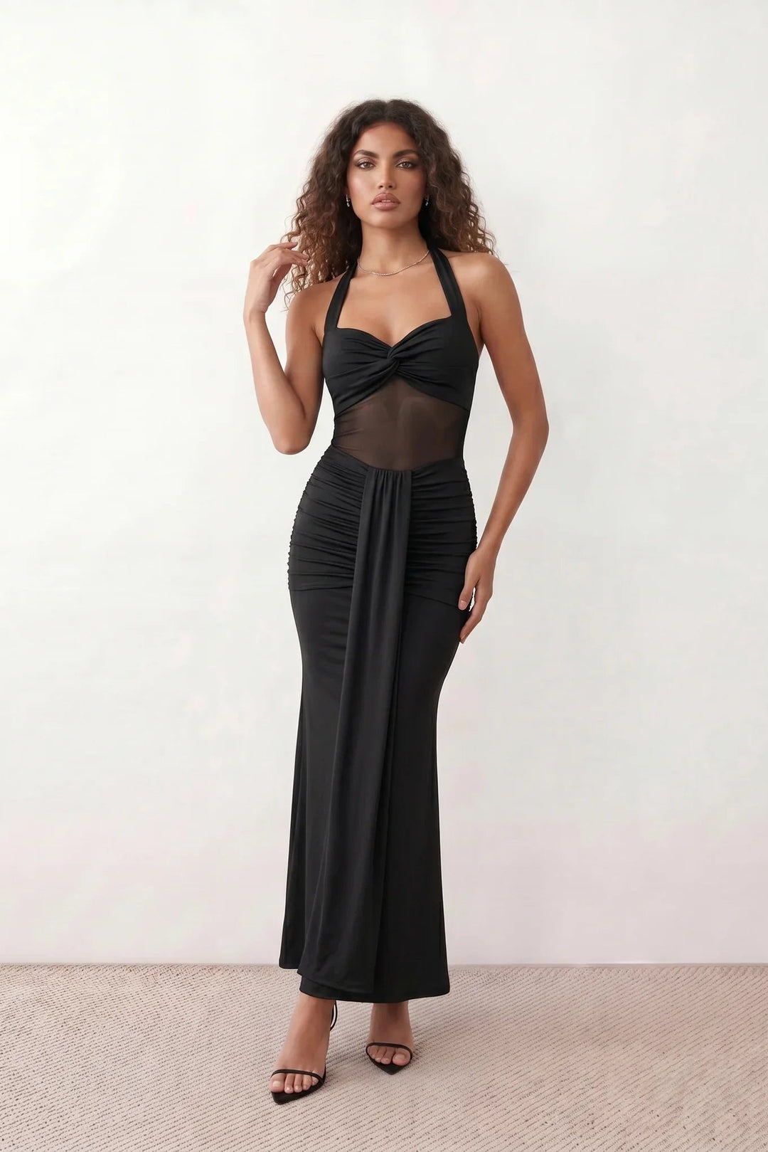 Woman wearing the Halter Neck Mermaid Maxi Dress featuring a sweetheart twist-knot neckline, sheer mesh waist panel, ruched mermaid silhouette, draped front skirt, open back with halter tie fastening, and elegant floor-length finish.